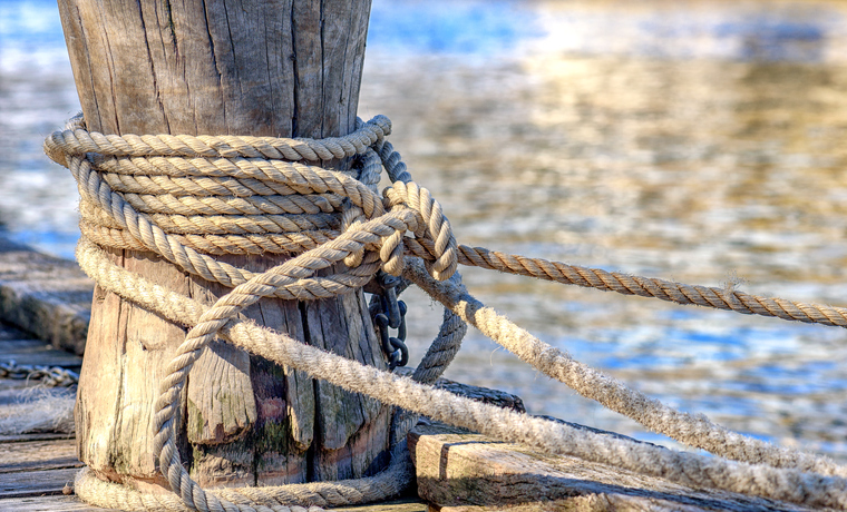 A rope is tied to a wooden mooring bollard with a reflective river in the background in Melbourne, Australia